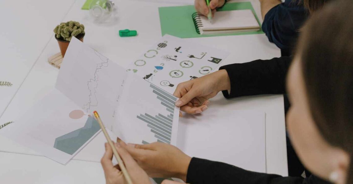 Equipa em reunião a analisar gráficos e indicadores relacionados com sustentabilidade, com documentos, apontamentos e elementos em tons de verde sobre a mesa.