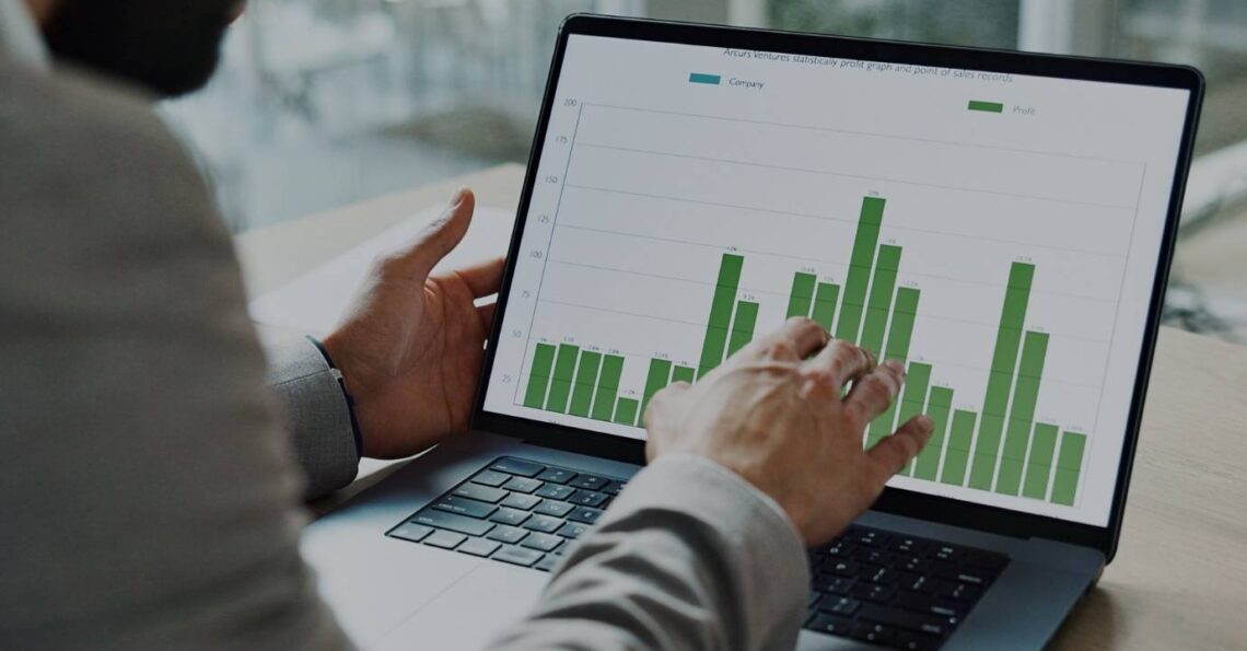 Pessoa a analisar um gráfico de barras verdes num portátil, num ambiente de escritório.