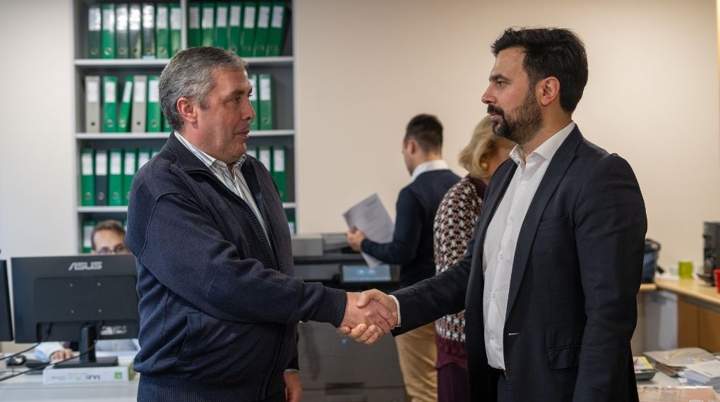 Aperto de mão entre consultor e cliente em ambiente de escritório, com estantes de arquivo em fundo, simbolizando a celebração de um acordo e a proximidade no acompanhamento do negócio.